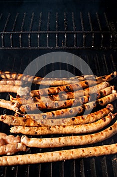Roasted sausages cooking on flaming grill barbecue with smoke.