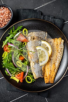 Roasted sea bass fillet with salad, Branzino fish. Black background. Top view