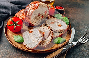 Roasted sliced pork ham on a wooden plate on a dark rustic background