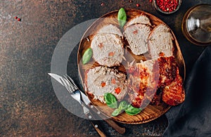 Roasted sliced pork ham on a wooden plate on a dark rustic background. Top view