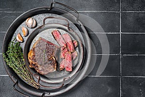 Roasted Sliced Wagyu New York beef meat steak or Striploin steak in a steel tray with herbs. Black background. Top view
