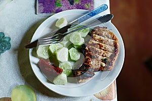 Roasted steak meat with bone, cucumber , ketchup fork and knife