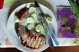 Roasted steak meat with bone, cucumber , ketchup fork and knife