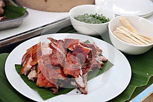 Roasted suckling pig, crispy skin, cut into pieces Looks delicious on a white plate, beneath the pork with banana leaves.