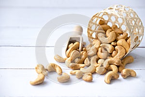 Roasted tasty cashew nuts in wooden spoon in bowl on a white  wooden table, isolated background with copyspace for your text photo