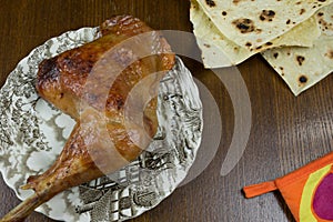 Roasted turkey leg on the printed grey plate on the wooden table and toasted bread by the side.