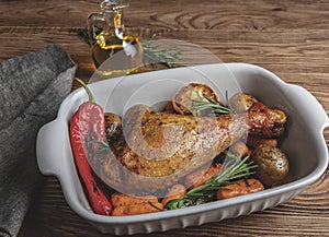 Roasted turkey leg with vegetables, carrots, peppers, potatoes in ceramic baking dish.