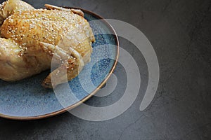Roasted whole chicken on a plate on the dark background.