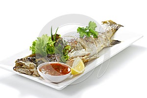 Roasted Whole Giant Sea Perch Fish Pra-Kra-Pong with Red Chili Garlic Seafood Sauce and a piece of lemon on white porcelain