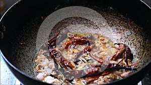 Roasting onions, dried red chilli and curry leaves in oil to make tadka. Tadka is used in Indian dishes to improve taste