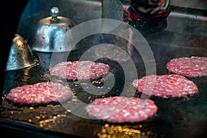 Roasting raw marbled beef burger patties on  iron grill