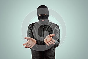 Robber, bandit in a balaclava surrenders on a light background. Robbery, hacker, crime, theft. Copy space