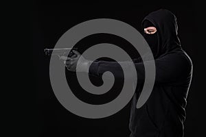 The robber in a mask with a gun pointed to the side on a black background