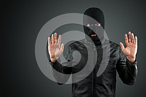 Robber, a thug in a balaclava raised his hands on a black background, surrenders. Robbery, hacker, crime, theft, arrest. Copy