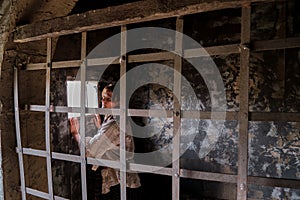 The robber woman looks at the sun through a small window from behind the bars of the prison