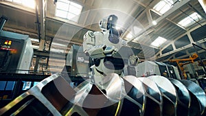 Robot checks metal detail at a factory, typing on a tablet.