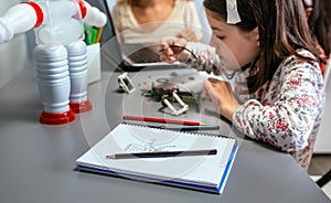 Robot draw by child on notebook and student connecting wire in electrical circuit on background