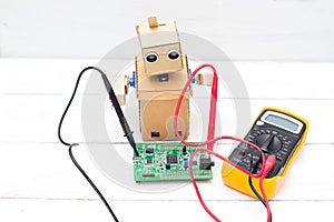 The robot holds a voltmeter in its hands and a printed circuit b