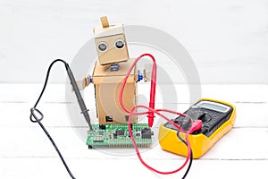 The robot holds a voltmeter in its hands and a printed circuit b