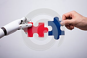 Robot And Human Hand Holding Jigsaw Puzzle