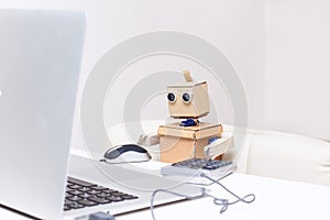 Robot is sitting at the table and working at a laptop