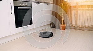 A robot vacuum cleaner in a bright modern kitchen on a white laminate background cleans up and makes a clean room