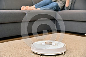 Robot vacuum cleaner cleaner the floor while woman uses her mobile smartphone, have rest and relaxation