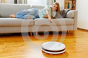 Robot vacuum cleaner cleaning a room while a woman relaxes on the sofa