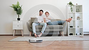 Robot vacuum cleaning floor while happy couple using laptop