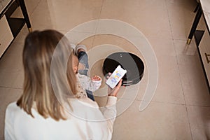 Robotic vacuum cleaner cleaning the room while mother relaxing with baby infant child. Woman controlling vacuum with