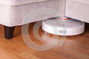 Robotic vacuum cleaner runs under sofa in room on laminate floor modern smart cleaning technology housekeeping