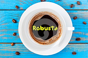 Robusta - sort of coffee, written on morning coffees mug at blue wooden table with beans