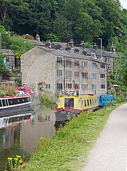 Canal running through hebden bridge with moored boats reflected in the water and stone buildings surrounded by trees