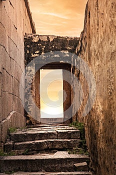 Rock Architecture Narrow ancient old street with stone steps to an open rock door with an open sky sunset