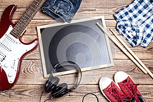 Rock background with music equipment, clothes and footwear on wooden table with clean blackboard.