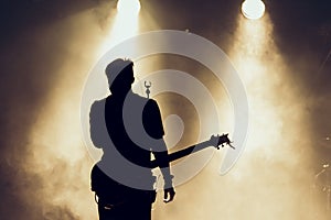 Rock band performs on stage. Guitarist plays solo. silhouette of guitar player in action on stage in front of concert crowd. Close