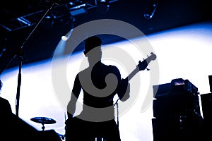 Rock band performs on stage. Guitarist plays solo. silhouette of guitar player in action on stage in front of concert crowd. Close