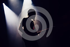 Rock band performs on stage. Guitarist plays solo. silhouette of guitar player in action on stage in front of concert crowd.