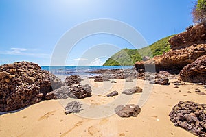 The rock on the beach sand and green mountain with blue sky midday