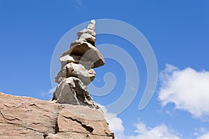 Rock cairn trail marker on boulder with blue sky