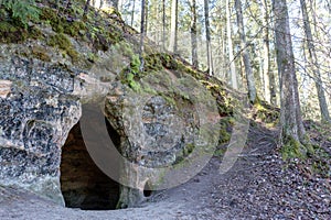 a rock cave in a wooded area with a walking path behind it