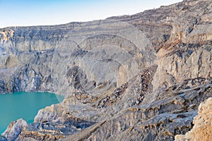 Rock cliff at Kawah Ijen volcano with turquoise sulfur water lake at sunrise. Panoramic view at East Java, Indonesia. Natural