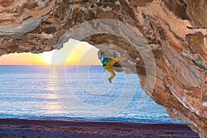 Rock Climber assaulting overhanging rocky Roof at Sea Beach Sunrise Background