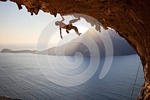 Rock climber climbing along roof in cave at sunset