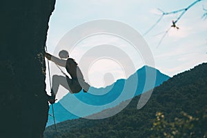 A rock climber climbs a rock against the background of mountains and sky