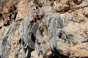 Rock climber girl in orange pants leaging climbing route on natural rock