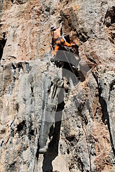 Rock climber girl in orange pants leaging climbing route on natural rock