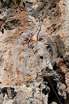 Rock climber girl in orange pants leaging climbing route on natural rock
