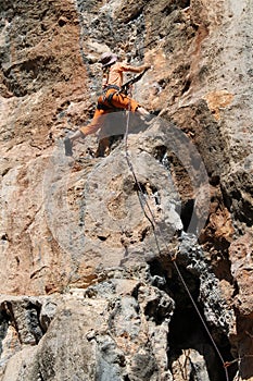 Rock climber girl in orange pants leaging climbing route on natural rock