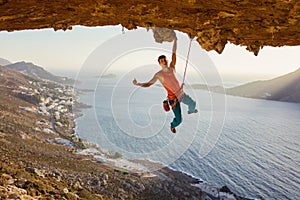 Rock climber hanging on cliff with one hand and showing thumb up